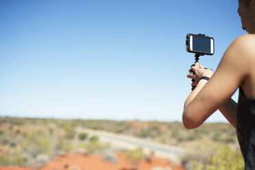 Woman photographing landscape against clear blue sky on sunny day - CAVF22831