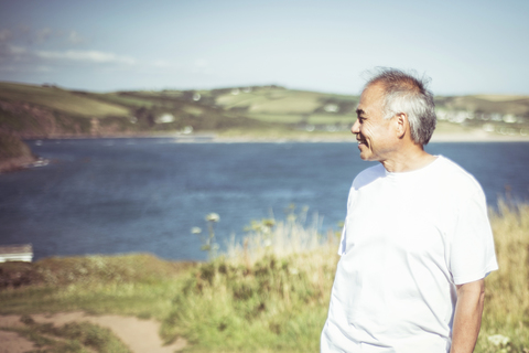 Älterer Mann schaut weg, während er auf einem Feld am See steht, lizenzfreies Stockfoto