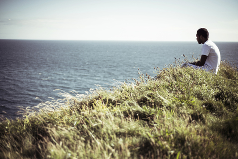 Seitenansicht eines Mannes, der auf einem Feld am See sitzt, lizenzfreies Stockfoto