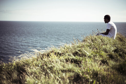 Seitenansicht eines Mannes, der auf einem Feld am See sitzt - CAVF22842