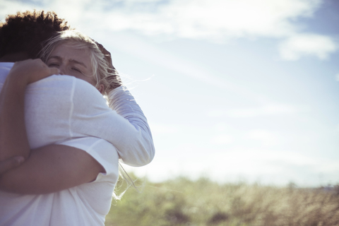 Paar umarmt auf Feld gegen Himmel, lizenzfreies Stockfoto