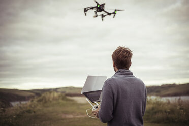 Rear view of man operating drone camera while standing on field - CAVF22853