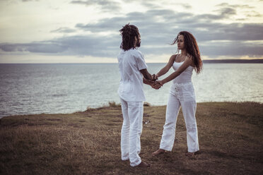 Couple holding hands while standing face to face on field - CAVF22857