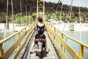 Rear view of woman riding scooter on bridge - CAVF22861