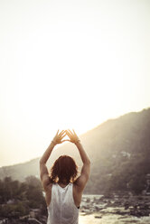 Rear view of woman with arms raised standing against clear sky - CAVF22885