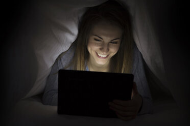 Glückliche Frau, die einen Laptop benutzt und in einer Decke liegt - CAVF22919