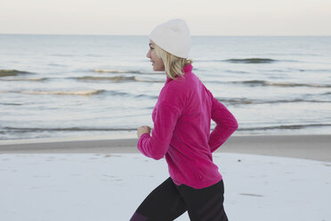 Side view of teenage girl jogging at beach against sea - CAVF22925