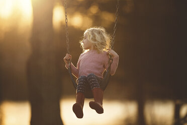 Mädchen spielt auf einer Schaukel auf einem Spielplatz bei Sonnenuntergang - CAVF22935