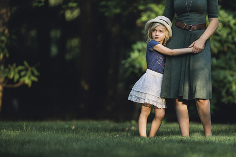 Nachdenkliches Mädchen mit Mutter auf einer Wiese stehend, lizenzfreies Stockfoto