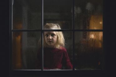 Portrait of thoughtful girl seen through wet glass window at night - CAVF22954