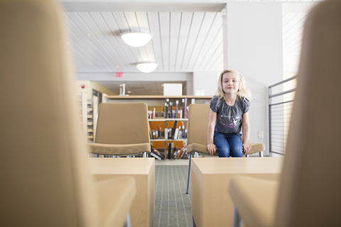 Porträt eines lächelnden Mädchens, das in einer Bibliothek auf einem Stuhl sitzt, lizenzfreies Stockfoto