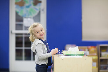 Porträt eines niedlichen lächelnden Mädchens, das an einem Tisch in der Schule steht - CAVF22958