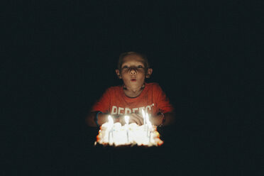 Niedlicher Junge bläst Geburtstagskerzen in der Dunkelkammer aus - CAVF22960