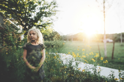 Nachdenkliches Mädchen steht inmitten von Pflanzen im Garten, lizenzfreies Stockfoto