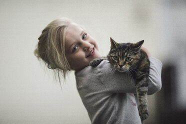 Porträt eines niedlichen Mädchens, das eine getigerte Katze zu Hause hält - CAVF22974