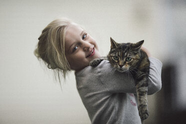 Portrait of cute girl holding tabby cat at home - CAVF22974