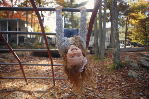 Porträt eines glücklichen Mädchens, das auf einem Spielplatz im Herbst auf einem Klettergerüst spielt - CAVF23035