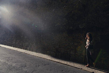 Sonnenlicht fällt auf eine Frau, die auf dem Gehweg an einer Mauer entlang läuft - CAVF23038