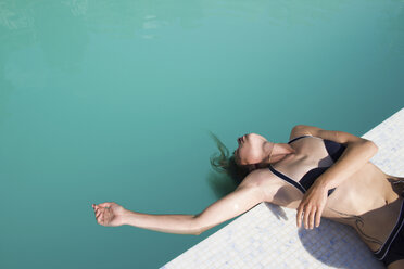 High angle view of woman lying on poolside with head in water - CAVF23074