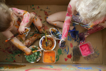 High angle view of siblings playing with paints while sitting in cardboard box - CAVF23088