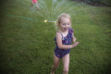 Girl playing with water on grassy field at backyard - CAVF23092