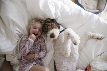 High angle portrait of cheerful girl relaxing with dog on bed at home - CAVF23100