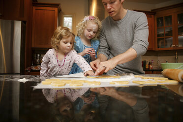 Father with daughters making cookies at table in kitchen - CAVF23111