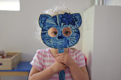 Porträt eines Mädchens, das eine Katzenmaske hält, während es zu Hause steht - CAVF23132