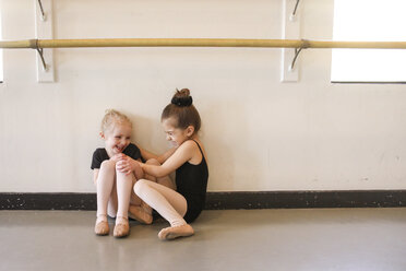 Playful girl tickling friend while sitting in ballet studio - CAVF23135