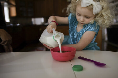 Mädchen gießt Milch in eine Schüssel auf dem Tisch - CAVF23169