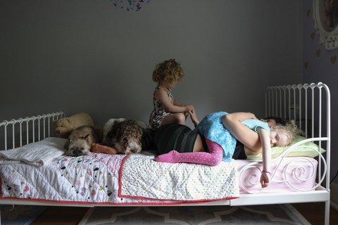 Töchter auf Mutter mit Hunden auf dem Bett liegend an der Wand zu Hause, lizenzfreies Stockfoto