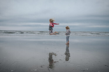 Carefree girl jumping while sister standing at beach against sky - CAVF23176