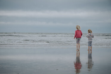 Rear view of sisters standing at beach against sky - CAVF23177