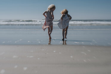 Rückansicht von Schwestern, die ein Kleid halten, während sie am Strand gegen den klaren Himmel laufen - CAVF23179