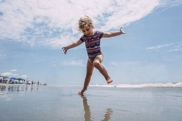 Low angle view of carefree girl playing at beach against cloudy sky - CAVF23197