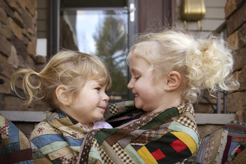 Glückliche Schwestern in Decken eingewickelt auf der Veranda, lizenzfreies Stockfoto