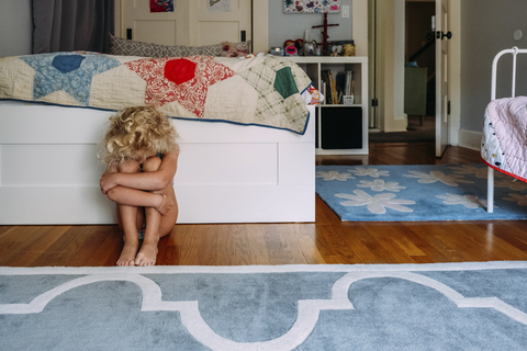 Trauriges Mädchen, das die Knie im Schlafzimmer umarmt, lizenzfreies Stockfoto