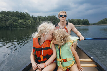 Sister kissing girl while father canoeing in lake against stormy clouds - CAVF23222