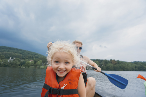 Glückliche Tochter im Kanu mit Vater Kanufahren im Hintergrund gegen stürmische Wolken, lizenzfreies Stockfoto