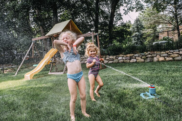 Happy sisters playing in sprinkler at park - CAVF23226