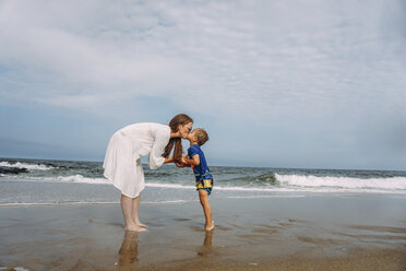 Mutter und Sohn küssen sich auf den Mund, während sie am Strand gegen den Himmel stehen - CAVF23233