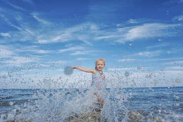 Portrait of playful girl splashing water while standing in sea against cloudy sky - CAVF23237