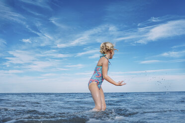 Side view of girl playing while standing in sea against cloudy sky - CAVF23238