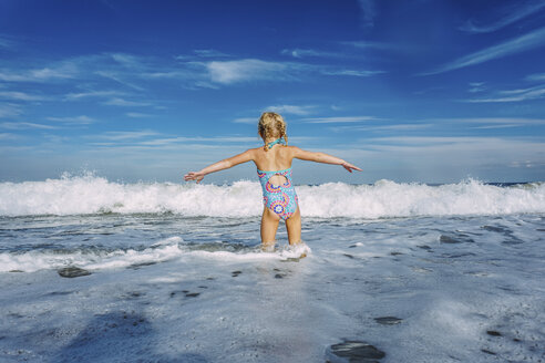 Rear view of girl with arms outstretched standing in sea against cloudy sky - CAVF23239