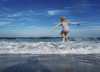 Full length of playful girl with arms outstretched jumping over shore against sky - CAVF23240