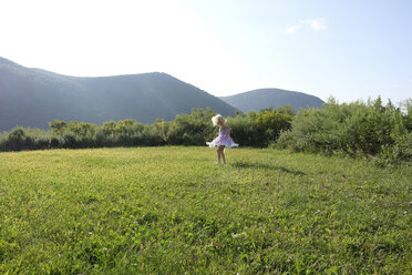 Verspieltes Mädchen, das sich auf einem grasbewachsenen Feld vor Bergen und Himmel dreht - CAVF23241