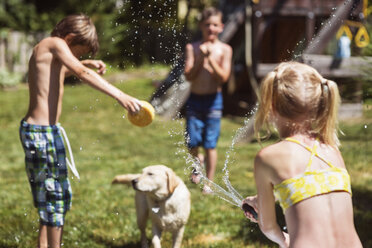 Rückansicht eines Mädchens, das seinen Hund und seine Freunde im Hinterhof mit Wasser bespritzt - CAVF23251
