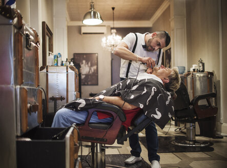 Barbier rasiert den Bart eines Mannes im Geschäft - CAVF23253
