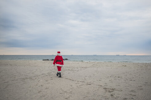 Rear view of senior man in Santa costume walking at beach - CAVF23254