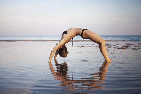 Frau im Bikini macht Yoga am Strand gegen den Himmel - CAVF23276